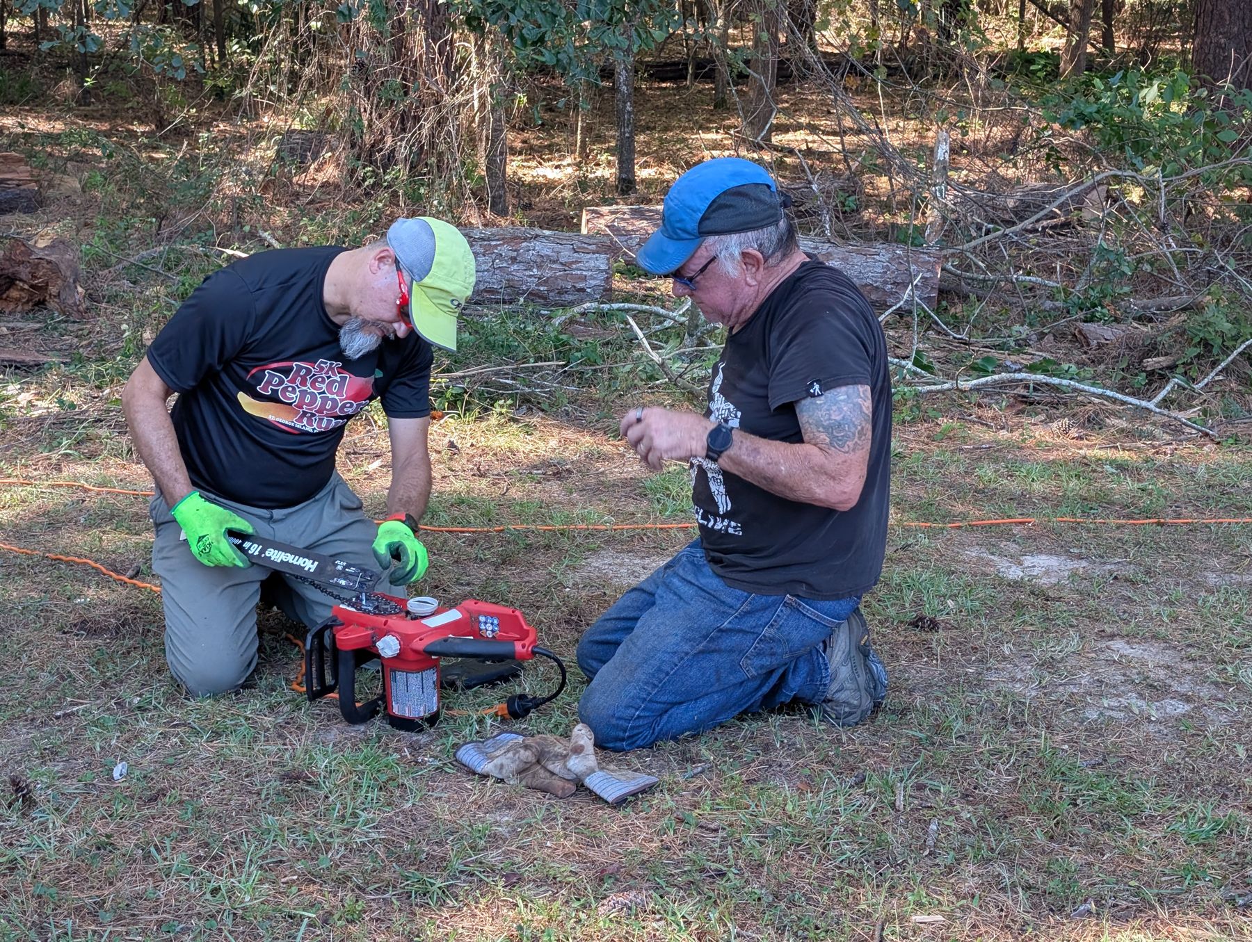 Two volunteers kneeling in a yard, working on a piece of equipment together