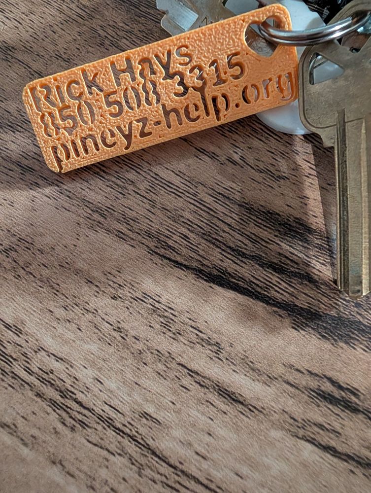 An orange 3D-printed keychain on a key ring reading Rick Hays, 850 508 3315, pineyz-help.org